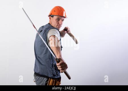 The builder shows a fight with a katana. Repairman wearing a helmet and work clothes. Stock Photo