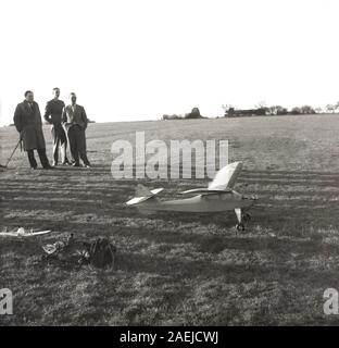 1950s, historical, a flying model aircraft on the ground outside on a grassy field, with enthusiast males looking on, England, UK. Stock Photo