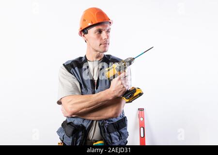 Builder repairman holding a drill like a gun. In a helmet and work clothes. Stock Photo