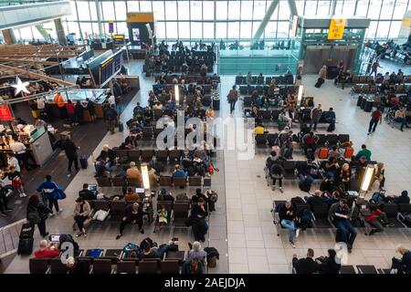 Passengers in a busy Heathrow Airport Terminal 5 Departures Lounge  sit in benches waiting for their flights. Stock Photo
