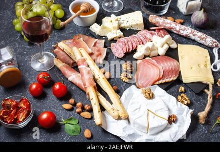 Italian antipasto with prosciutto, ham, cheese, olives and grissini breadsticks on black stone background. Stock Photo