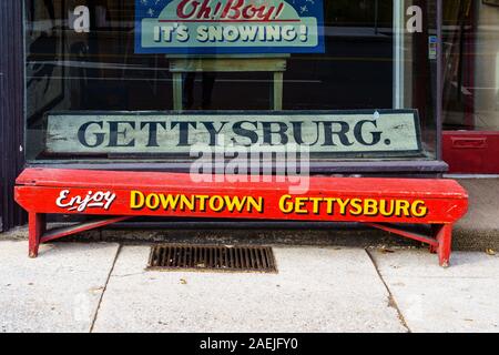 Gettysburg, PA / USA - December 7, 2019:  A red painted Bench with writing that invites to Enjoy Downtown Gettysburg in front of a store. Stock Photo