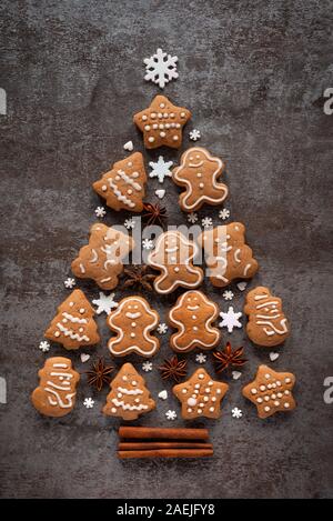 Gingerbread, anise stars and cinnamon sticks create a Christmas tree on a dark stone background Stock Photo