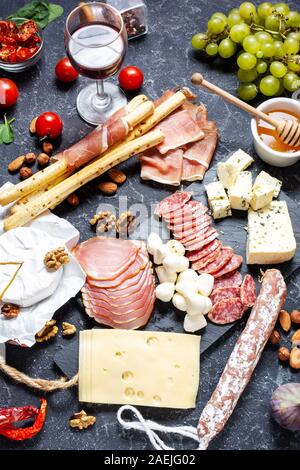 Italian antipasto with prosciutto, ham, cheese, olives and grissini breadsticks on black stone background. Stock Photo