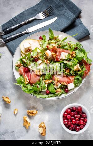 Green salad with arugula, pear, jamon and feta cheese on concrete background. Healthy food Stock Photo