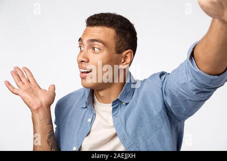 Handsome male in casual outfit record vlog from christmas travel, hold camera one stretch hand, introduce someone or pointing left, tell story as Stock Photo