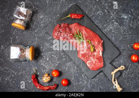 Raw fresh marbled meat Steak and seasonings on dark stone background. Top view Stock Photo