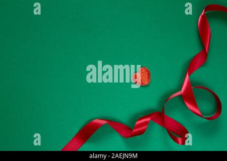 Delicate red ribbon and heart figure isolated on green background, Christmas or Valentine's Day holidays decoration concept Stock Photo
