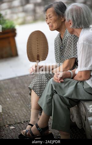 Guilin, China -  August 2019 : Portrait of two old retired chinese asian women sitting on a bench by the Shan Lake in a park  in summer Stock Photo