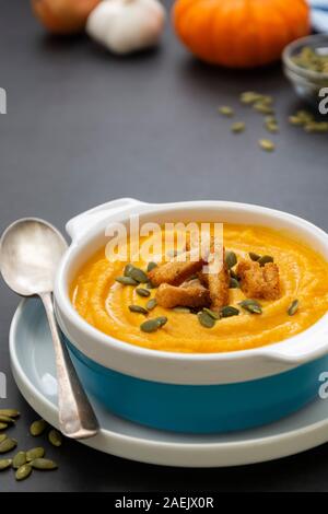 Creamy carrot soup, autumn foods. Spicy, roasted vegetable soup in bowl. Dark board. Stock Photo