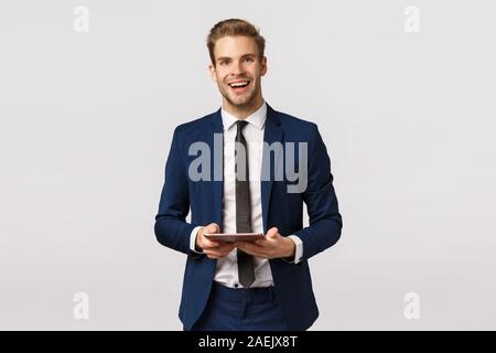 Cheerful, elegant bearded businessman in classic suit and tie, holding digital tablet laughing and smiling enthusiastic, having business plan written Stock Photo
