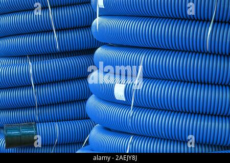 Coils of new red plastic pipe with rain drops. Red plastic tubing for underground cable protection. First floor of a skein of red corrugated tube. Pla Stock Photo