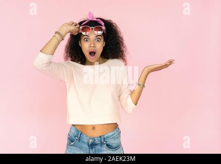 Shocked young teen african girl hold copy space isolated on pink wall Stock Photo picture