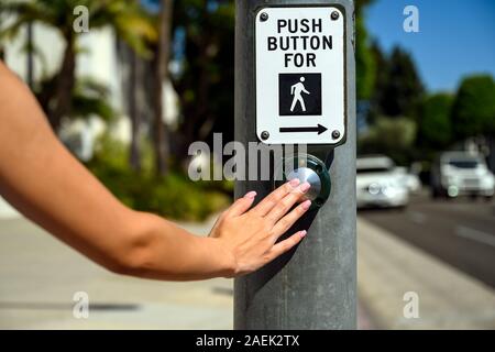 Push button to cross with sign, hand. Pedestrian crossing crosswalk. Female pushing a button to stop car traffic in an intersection. Stock Photo