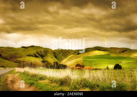 Dramatic sky and cloudscape above the rural agricultural farmland with a backdrop of a wind farm and turbines on the top of the hills Stock Photo