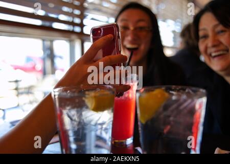 Middletown, CT USA. Mar 2019. Smartphone in hand showing reacting family or friends at a restaurant showing something funny online. Stock Photo