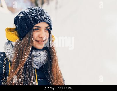 Winter portrait of young beautiful woman wearing knitted snood covered in snow. Snowing winter beauty fashion concept Stock Photo