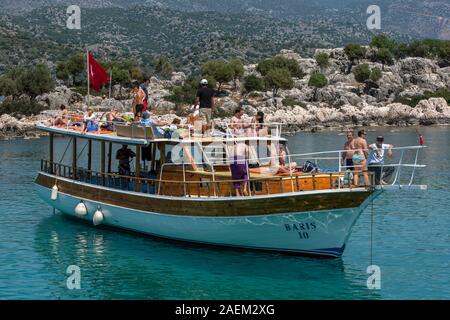 Tourists aboard a cruise boat enjoy the spring time hot weather whilst exploring adjacent to the Sunken City of Simena near Kekova Island in Turkey. Stock Photo