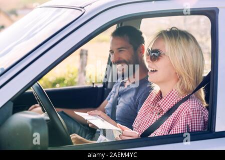 Happy couple traveling by car in nature and looking in map. Carefree friend travelers on countryside roadtrip journey. Young woman and man driving to Stock Photo