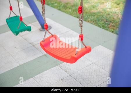 Plastic and Empty red and green chain swings in children playground. chain swings hanging in garden . Childs swing in a park . Stock Photo