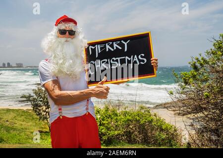 Santa Claus holds gift boxes with the ocean on backgraund. Australia, Christmas in summer time. Stock Photo