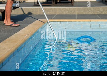 Male cleaning outdoor swimming pool with underwater vacuum tube Stock Photo