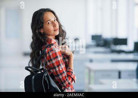 Computer screens behind. Portrait of attractive young woman standing in the office with black bag Stock Photo