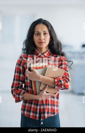 Vertical photo of attractive young woman standing in the office and holding books and documents Stock Photo