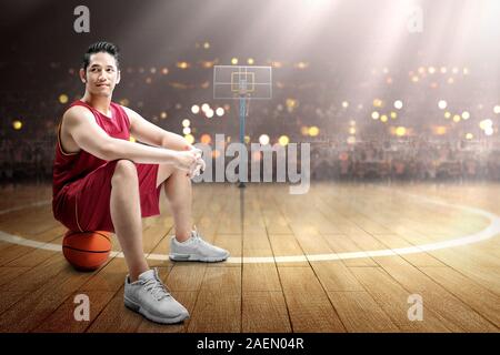Asian man basketball player sitting on the ball on the basketball court Stock Photo