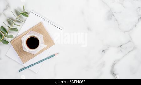 Home office desk with paper notepad, cup of coffee and eucalyptus leaf on marble background. Feminine workspace concept. Flat lay, top view, copy spac Stock Photo
