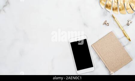 Marble desk table with beauty blogger fashion accessories and supplies. Home office workspace with mobile phone mockup, golden paper notebook, tropica Stock Photo