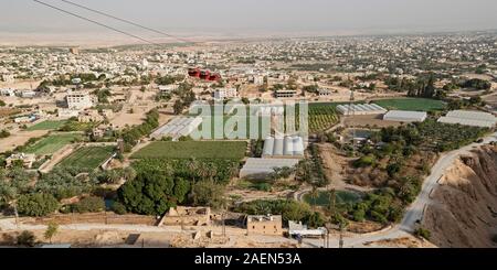 red cable cars going up to the mount of the temptation of jesus in jericho with modern high tech farms in the foreground and the palestinian city in t Stock Photo