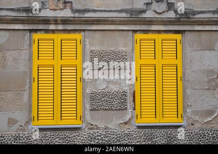 Yellow closed shutters on old grey building Stock Photo