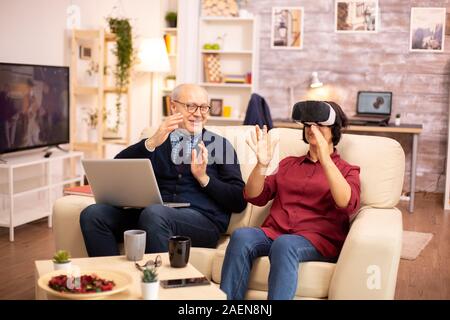 Old elderly retired woman in her 60s experiencing virtual reality for the first time in their cozy apartment Stock Photo
