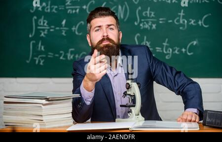 Educational conversation. Talking to students or pupils. School teacher concept. Teacher bearded man tell interesting story. Teacher charismatic hipster sit at table classroom chalkboard background. Stock Photo