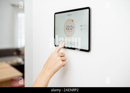Controlling temperature in the living room with a digital touch screen panel installed on the wall. Concept of heating control in a smart home, close-up on a screen Stock Photo