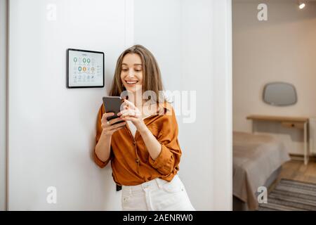 Young woman controlling temperature in the living room with smart phone and digital touch screen panel. Concept of heating control in a smart home Stock Photo
