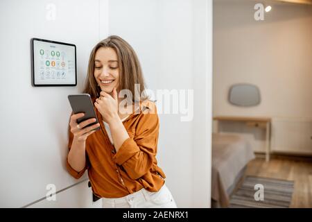 Young woman controlling temperature in the living room with smart phone and digital touch screen panel. Concept of heating control in a smart home Stock Photo