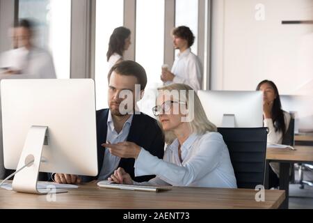 Mature businesswoman mentor teaching intern, using computer together Stock Photo