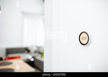 Round smart thermostat with touch screen installed on the wall indoors. Smart home heating regulation concept. View with copy space Stock Photo