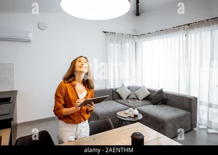 Young woman controlling home light with a digital tablet in the living room. Concept of a smart home and light control with mobile devices Stock Photo