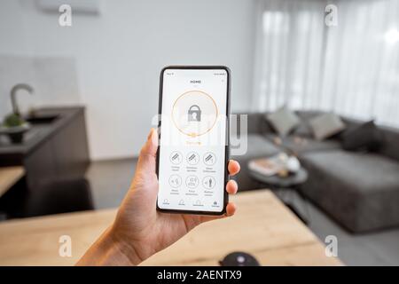 Holding a smartphone with launched security program indoors. Concept of controlling and managing home security from a mobile device Stock Photo