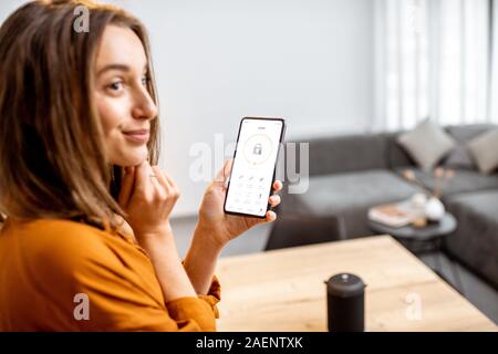 Young woman holding smart phone with launched security application at home. Concept of controlling and managing home security from a mobile device Stock Photo