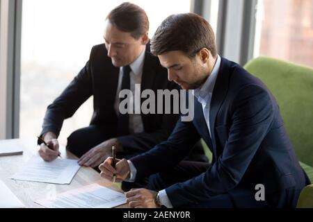 Successful businessmen in suits signing contract, partnership agreement