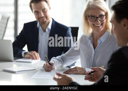 Smiling mature businesswoman signing contract, agreement at meeting Stock Photo