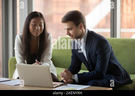 Smiling Asian businesswoman and businessman using laptop together Stock Photo