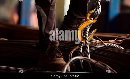 Worker loading rebar and hanging the load on the crane's chains in metalworking factory. Concept for industrial worker, manual work and manufacturing. Stock Photo
