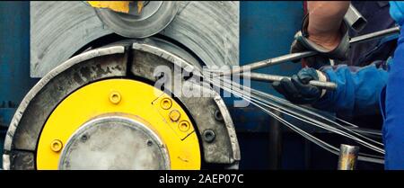 Worker holding a metal stake against a manufacturing machine for slitting/cutting/stripping steel sheets in the factory. Concept for metalwork product Stock Photo