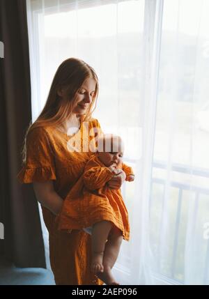 Mother with daughter infant baby at home family lifestyle mom and child together looking out window maternity concept Mothers day holiday dress clothi Stock Photo