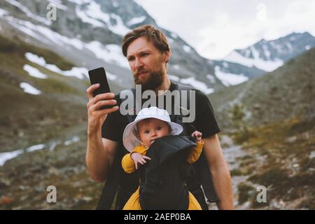 Travel family father and daughter baby carrier hiking in mountains adventure vacations with child man with smartphone checking gps navigation applicat Stock Photo